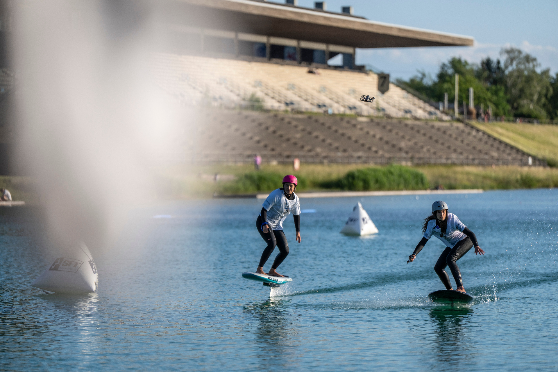 Zwei Riderinnen auf Foilboards vor der olympischen Regattaanlage